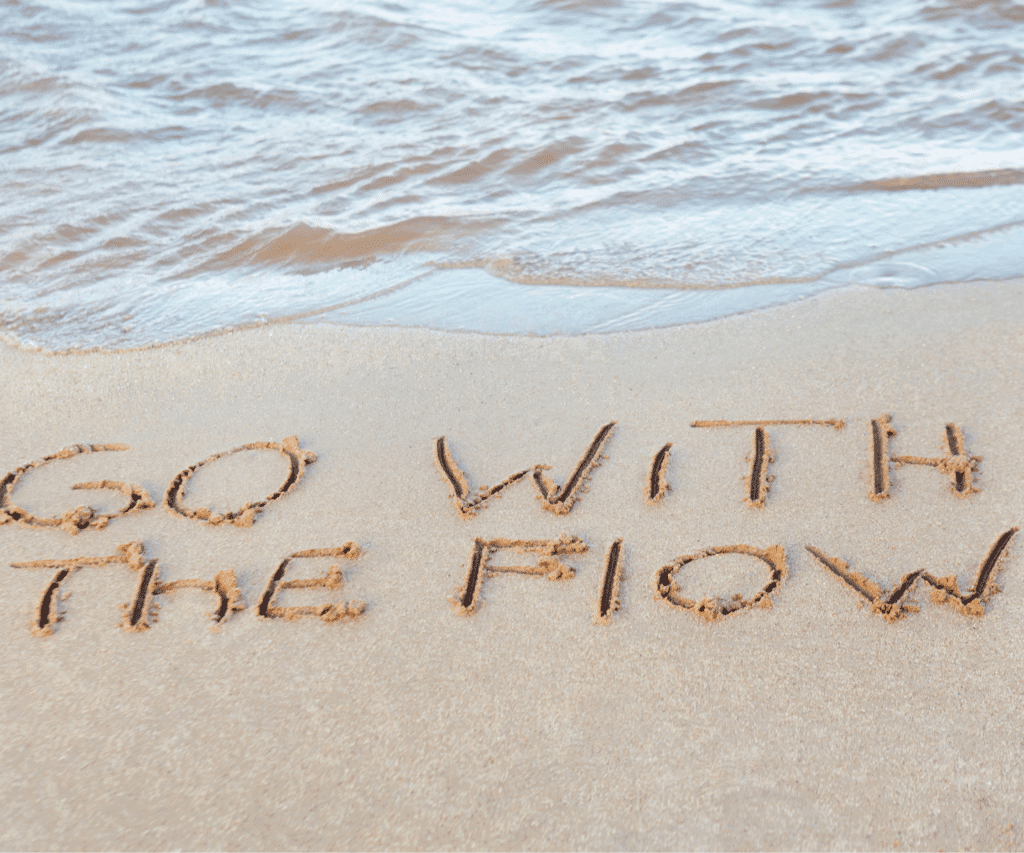 Schriftzug ‚Go with the flow‘ im Sand am Strand – Symbol für Leichtigkeit und Flow-Zustand – Mentaltraining Sandra Freidl