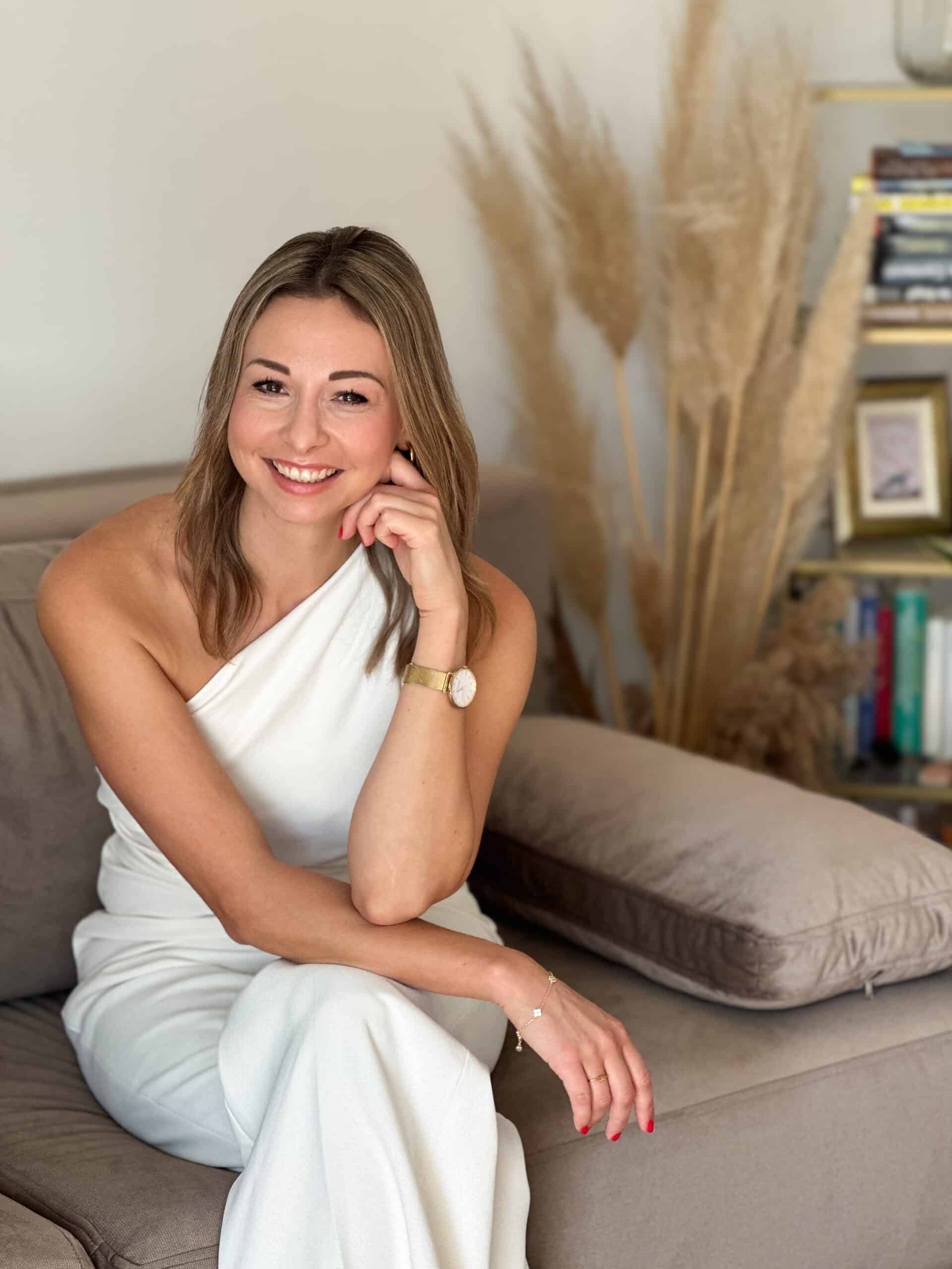 Sandra Freidl Mentaltrainerin aus Graz sitzt lächelnd auf einem Sofa – Portrait für Mentaltraining Website