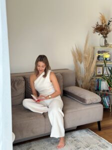 Frau sitzt auf einem Sofa und liest ein Buch – entspannter Moment für persönliche Entwicklung, mentale Gesundheit und Reflexion