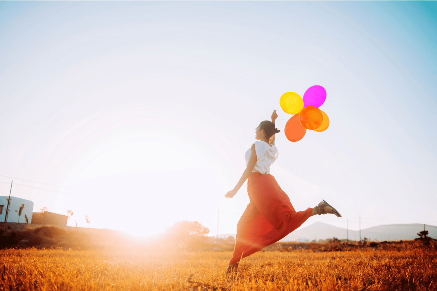 Frau springt auf einer Wiese mit bunten Luftballons – Symbol für Leichtigkeit, Freude und Glück.